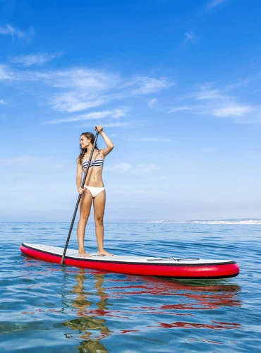 Woman stand-up paddling on calm blue waters under a clear sky.